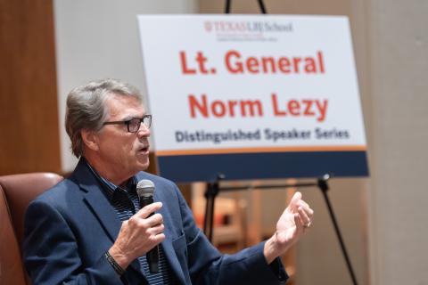 Rick Perry speaks to an audience with a sign that says "Lt. General Norm Lezy" behind him.